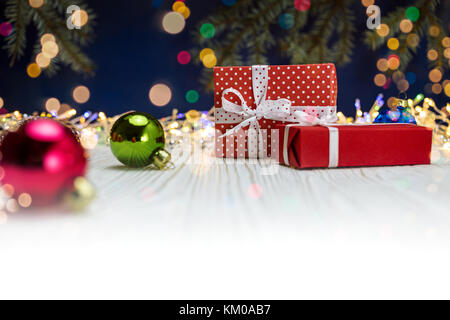 Cadeaux rouge et boules de verre coloré sur fond en bois blanc avec des lumières floues Banque D'Images