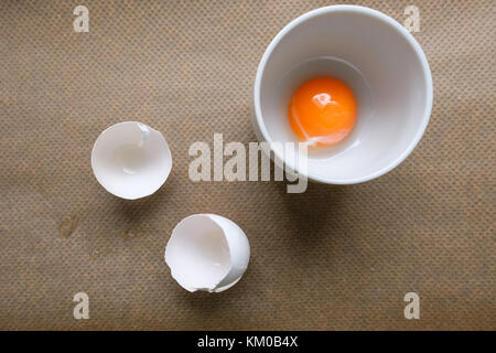 D'œuf dans une tasse et coquilles d'œufs blancs sur le papier parchemin Banque D'Images