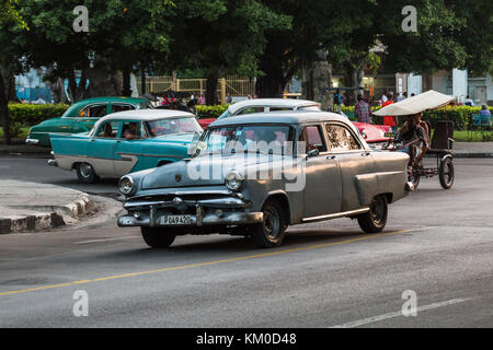 Un bicitaxi et quatre voitures classique américaine à partir des années 1950, capturé dans une trame serrée au coucher du soleil un soir d'août 2014 dans les rues de La Havane. Banque D'Images