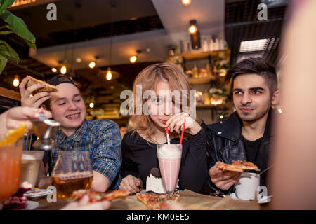 Jeune femme à boire le lait frappé alors qu'il était assis avec des amis au café Banque D'Images
