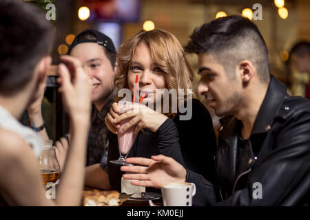 Jeune femme à boire le lait frappé alors qu'il était assis avec des amis au café Banque D'Images