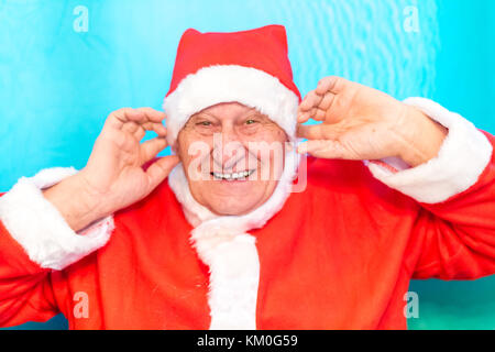 Vieux homme portant costume père noël boucher ses oreilles avec les doigts Banque D'Images