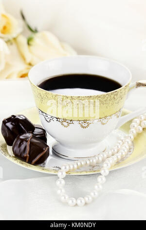 Gros plan d'une tasse de café au chocolat et collier de perle. roses dans l'arrière-plan. faible profondeur de champ. Banque D'Images