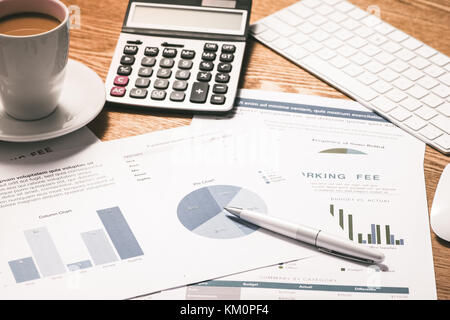 Graphiques et tableaux d'affaires sur un bureau en bois avec une calculatrice, stylo et tasse à café Banque D'Images