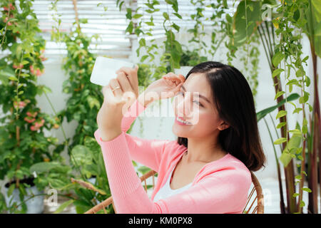 Cute asian girl prend des photos et des selfies assis dans le jardin ensoleillé. Banque D'Images