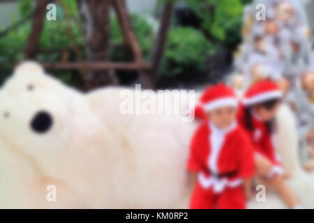 Image floue et hors du foyer pour l'arrière-plan de Little Boy and Girl dans de jolies tenues de Père Noël jouant avec un jouet Big Polar Bear Toy Banque D'Images