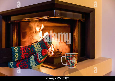 Pieds de chaussettes de laine par le Foyer de Noël. les jambes dans des bas de laine à un foyer de noël moderne. close up sur pieds. L'hiver et les vacances de Noël Banque D'Images