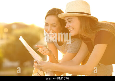 Deux touristes drôle de lire une carte en papier dans un hôtel balcon en vacances au coucher du soleil Banque D'Images