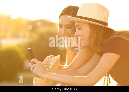 Deux amis regardent à la joyeuse contenu en ligne d'un téléphone intelligent à un balcon au coucher du soleil Banque D'Images