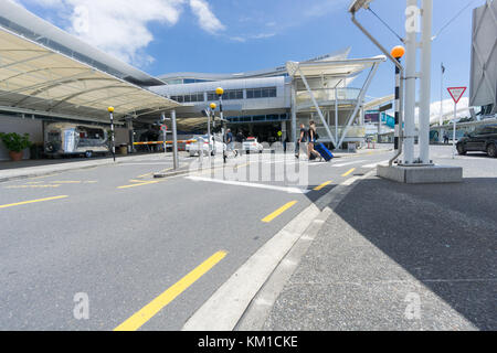 AUCKLAND, NOUVELLE-ZÉLANDE - 23 NOVEMBRE 2017 personnes, y compris un jeune couple tirant des cas de combinaison traversant la route vers l'entrée de l'aéroport international t Banque D'Images