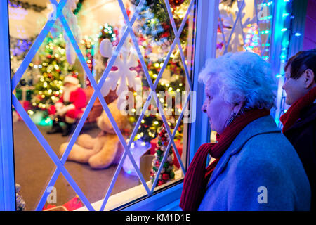 Les gens de la scène de Noël, les décorations, la femme âgée, les cheveux gris, regardant à l'intérieur de la maison du Père Noël à travers une fenêtre décorée de Noël Banque D'Images