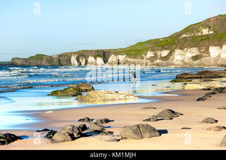 Les Roches Blanches également appelé East Strand à Portrush. Le Château de Dunluce à distance. L'homme pêche en mer. Le comté d'Antrim en Irlande du Nord Banque D'Images