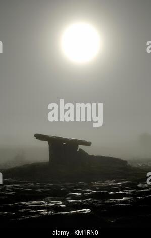 Lever de lune au lever du soleil dans le brouillard au-dessus de Poulnabrone preistoric Stone Age dolmen Tomb. Plateau calcaire de Burren, comté de Clare, Irlande Banque D'Images