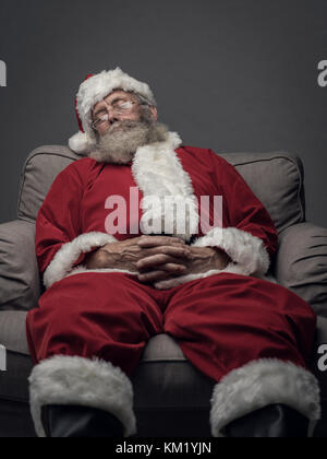 Sleepy santa claus prendre une sieste et reposant sur le fauteuil la veille de Noël Banque D'Images