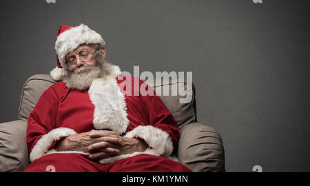 Sleepy santa claus prendre une sieste et reposant sur le fauteuil la veille de Noël Banque D'Images