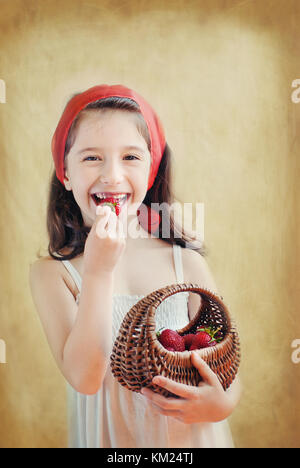 Portrait studio d'une petite fille tenant un panier de fraises et mangeant une fraise. Look vintage, image créative Banque D'Images