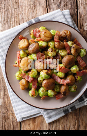 Délicieux apéritif : châtaignes grillées, choux de Bruxelles et lardons close-up sur une plaque sur une table. vertical haut Vue de dessus Banque D'Images