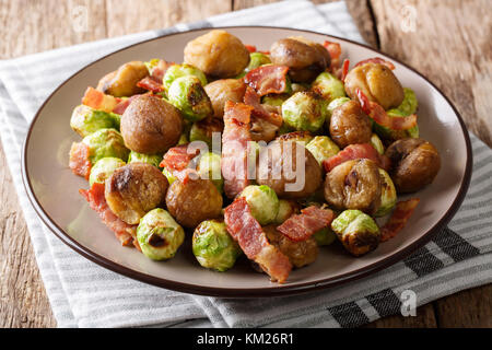 Délicieux apéritif : châtaignes grillées, choux de Bruxelles et lardons close-up sur une plaque sur une table horizontale. Banque D'Images