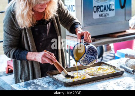 Une femelle baker prépare focaccia pain plat italien à un décrochage de plein air il est jeter de l'huile sur le dessus de la pâte avant il est placé dans un four à cuire Banque D'Images