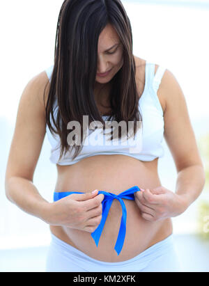 Close up of a smiling pregnant woman attacher un ruban bleu sur son ventre. Banque D'Images