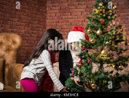 3 enfants indiens mignons décorant arbre de noël tout en portant chapeau de clause santa Banque D'Images