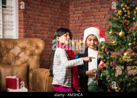 3 enfants indiens mignons décorant arbre de noël tout en portant chapeau de clause santa Banque D'Images