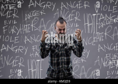 Homme qui crie en colère pleins de rage et de haine de griffer l'air de ses mains serrées avec un tag cloud mot avait écrit couvrant ses émotions sur un chalkbo Banque D'Images