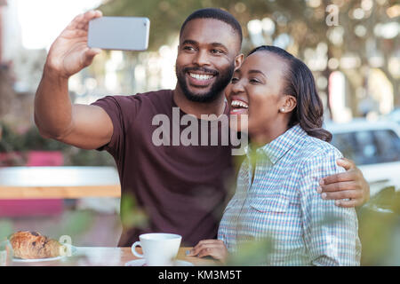 Laughing young African couple taking autoportraits à un sidewalk cafe Banque D'Images