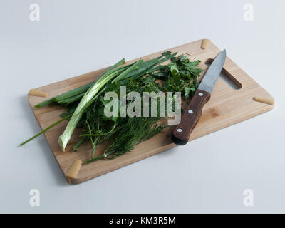 Aneth, persil, oignons verts se trouvent sur la planche à découper cuisine ensemble et couper en morceaux avec un couteau Banque D'Images