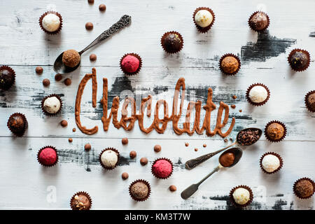 Chocolat mot fabriqué à partir de vitrage avec des chocolats, bonbons et petites cuillères en bois blanc sur un arrière-plan. Typographie alimentaire concept. Banque D'Images