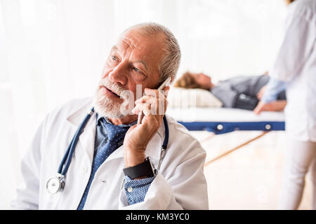 Médecin senior avec le smartphone dans son bureau. Banque D'Images