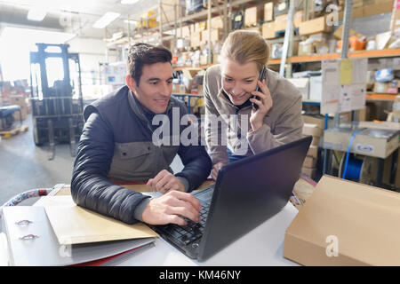 Les gestionnaires qui travaillent sur ordinateur portable et parlant au téléphone dans l'entrepôt Banque D'Images