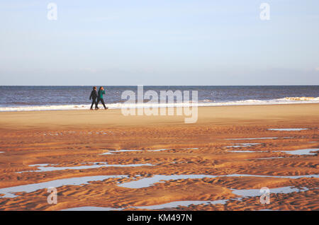 Une vue de deux jeunes femmes marchant près du bord de mer sur la côte nord du Norfolk à East Runton, Norfolk, Angleterre, Royaume-Uni. Banque D'Images