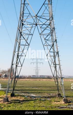 Une rangée de pylônes à haute tension sont debout dans un domaine rural et contre un ciel bleu dans les Pays-Bas. Banque D'Images