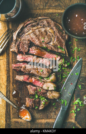 Télévision à jeter de rosé Ribeye Steak de boeuf coupé en morceaux sur la planche de bois rustique avec chutney de mangue et sauce vin rouge dans le verre, vue d'en haut Banque D'Images