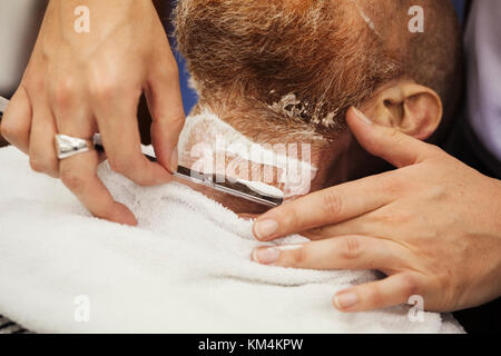 Un client assis dans le coiffeur, ayant un rasage humide par un salon de coiffure à l'aide d'un rasoir coupe gorge. Banque D'Images