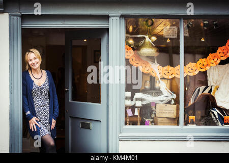 Une femme debout sur le seuil de sa pop up boutique de design d'intérieur avec une fenêtre d'affichage des objets. Banque D'Images