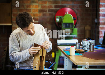 Un artisan dans un atelier, ou cordon d'Enfilage ficelle à travers un petit objet fait main. Banque D'Images