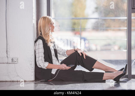 Businesswoman sitting on floor et de charge téléphone Banque D'Images