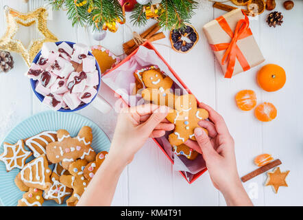 Vue supérieure de la femme met les mains de Noël traditionnel fait main gingerbread man cookies dans boîte cadeau. table en bois blanc avec décoration de Noël concept. s. Banque D'Images