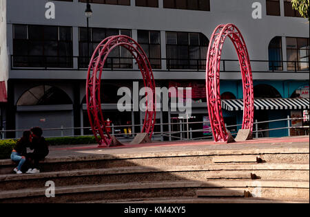 Deux roues rouges forment l'art dans une plaza square, San Jose, Costa Rica derrière young couple Banque D'Images