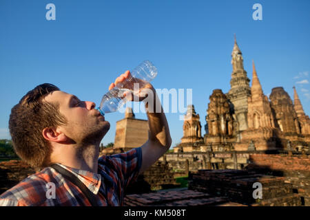 Jeune homme est assoiffé de l'eau en bouteille de boisson dans le bouddhisme en Thaïlande le temple du beau temps chaud Banque D'Images