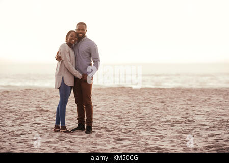 Smiling young couple debout sur une plage au coucher du soleil Banque D'Images