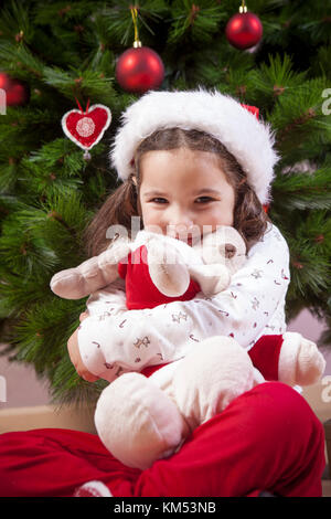 Petite fille embrassant son jouet de renne moelleux près de l'arbre de Noël.Elle est très, très heureuse Banque D'Images