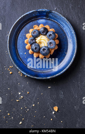 Vue de dessus sur le bleuet mini tartelette servi sur une plaque en céramique bleu foncé sur fond de pierre. Banque D'Images