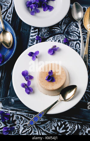 Vue de dessus sur la plaque avec pannacotta caramel servi avec des fleurs violettes sur fond noir et blanc Banque D'Images