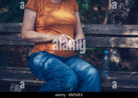 Pregnant woman texting outdoors on park bench, adulte femelle de race blanche à l'aide de téléphone mobile pendant la grossesse Banque D'Images