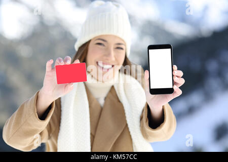 Vue avant, portrait d'une femme montrant une carte et l'écran du téléphone dans une montagne enneigée en hiver Banque D'Images