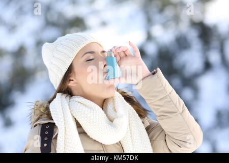 Portrait d'une femme à l'aide d'un inhalateur d'asthme dans un hiver froid avec la montagne enneigée en arrière-plan Banque D'Images