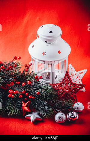 Lanterne blanc noël est debout avec une bougie allumée à l'aide d'une branche de sapin, et tricoter étoile en face de lui sur un fond rouge. fa noël Banque D'Images